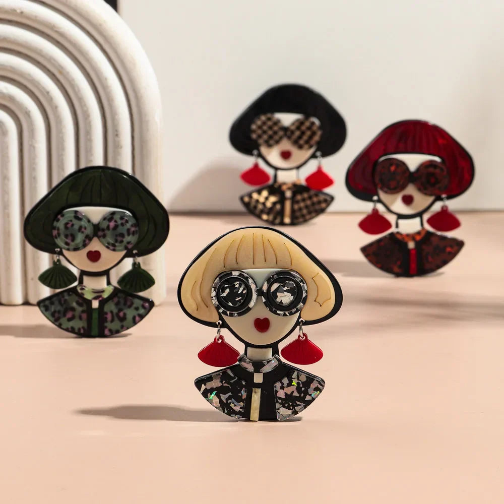 Four different colored broaches of women with glasses on wearing large earrings.