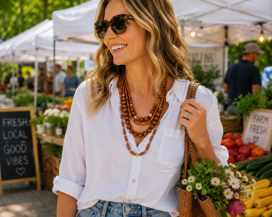 Woman wearing a bold Wildwood Whimsy wooden statement necklace with a casual white shirt while shopping at an outdoor farmers market.